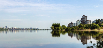 Город на водохранилище / Утром в мае с берега водохранилища. Край берега и городской массив справа. Вдали другой правый берег и город.. Отражения берегов в водной глади утром.