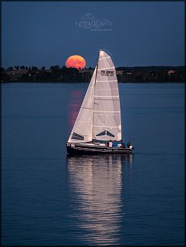 Full Moon Rising / Full moon rise with reflection in the lake against the background of a sailing yacht