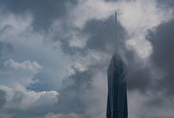 &nbsp; / The Merdeka 118 Tower in Kuala Lumpur, Malaysia, rises through dramatic clouds, with its sleek glass facade and spire piercing the sky. The moody atmosphere and partially obscured view highlight the tower’s height and architectural elegance against a backdrop of swirling clouds.