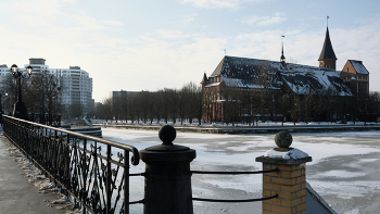 Кафедральный собор на о. Канта / Калининград. Вид на Кафедральный собор с "Деревянного моста". Кафедральный собор (До́мский собо́р Богома́тери и Свято́го Адальбе́рта) датой завершения строительства которого считается 1380 год, построенный в стиле кирпичной (балтийской) готики. Службы в соборе не проводятся, здание используется для размещения музейных экспозиций и проведения концертов. На правом углу, обращенном в сторону моста виден открытый колонный зал, внутри которого стоит каменный гроб, который является кенотафом останков И. Канта, но сами останки покоятся немного глубже.