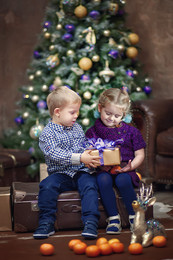 Новогодние подарки / Мальчик и девочка под Новогодней елкой обмениваются подарками
