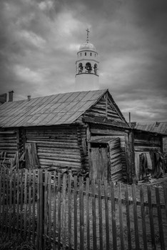 Монастырь в центре села. / Деревенская постройка на фоне колокольни монастыря .