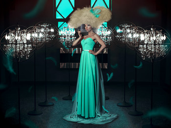 &nbsp; / Woman in a teal dress wearing a bird cage through huge blond hair among several lights